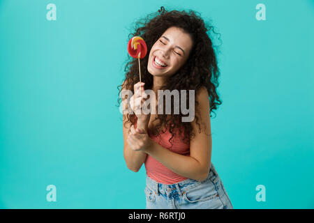 Portrait of beautiful woman 20s wearing casual clothing holding lollipop isolated over blue background Stock Photo