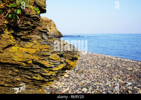 Rock close up against the background of the sea and pebble beach. Behind the cliffs is a seashore and blue water. East of Russia, the city of Vladivos Stock Photo