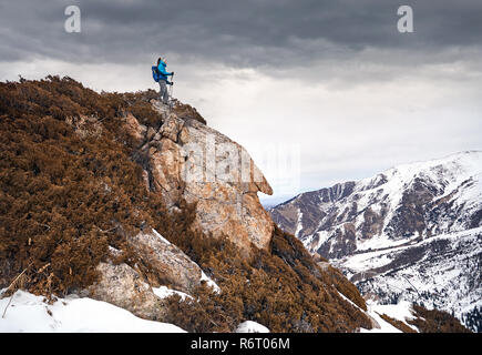 Tourist with dreadlocks climbs the rock at snowy mountains background Stock Photo