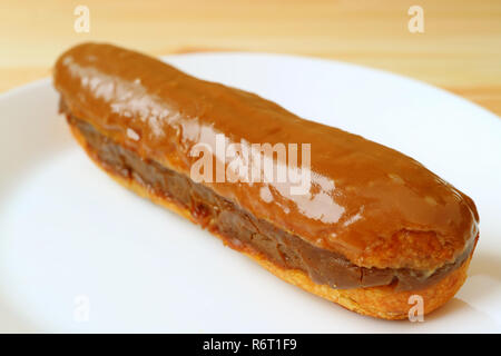 Close Up Mouthwatering Caramel Eclair Filled with Chocolate Served on White Plate Stock Photo