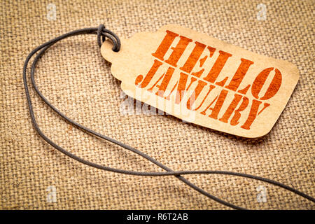 Hello January  - a paper price tag with a twine against burlap canvas Stock Photo