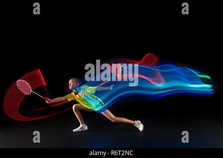 The one caucasian young teenager girl playing badminton at studio. The female teen player on black background in motion with flashes of light Stock Photo