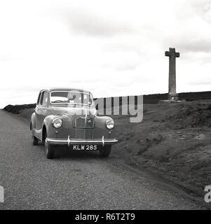 1950s, historical, a motorcar of the era parked on a road on a hillside, beside a stone cross, Ireland Stock Photo