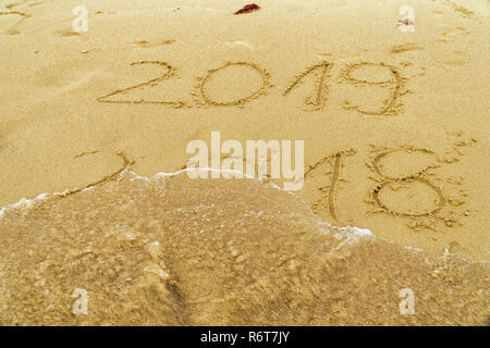 New Year 2019 is coming concept - inscription 2018 and 2019 on a beach sand, the wave is  covering the digits 2018. Stock Photo