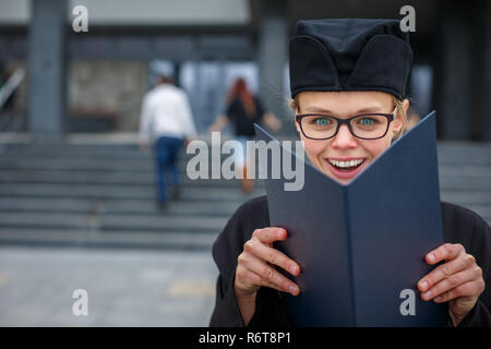 Pretty, young woman celebrating joyfully her graduation - cheking her diploma, happy/impressed with the title she received (color toned image  shallow DOF) Stock Photo
