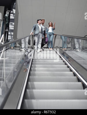 businesspeople moving down on escalator in office Stock Photo