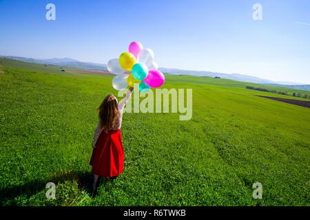 Happy girl in the meadows tuscan with colorful balloons, against the blue sky and green meadow. Tuscany, Italy Stock Photo