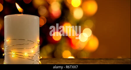 Illuminated string lights wrapped on lit candle against two red christmas balls on a white fur Stock Photo