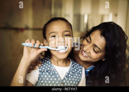 Portrait of girl brushing teeth with mother in bathroom Stock Photo