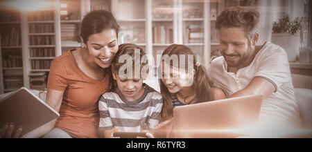 Happy family using technologies while sitting on sofa at home Stock Photo