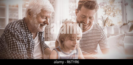 Boy using digital tablet with his father and grandfather in living room Stock Photo