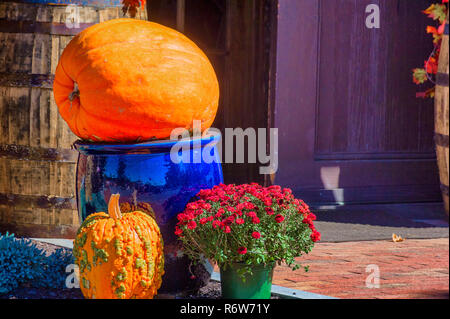 A large orange pumpkins sits on a tall blue planter with a smaller orage and green pumpkin and red mums set at the base of the large ceramic blue pla Stock Photo