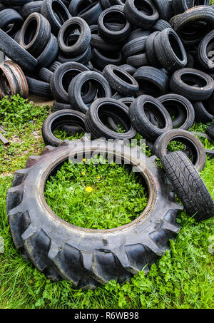 pile of worn car and tractor tires piled up in a grass field Stock Photo