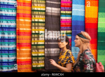 Marrakech tourists - women walking past colourful fabrics in the souk, Marrakech Medina, Marrakesh, Morocco Africa Stock Photo