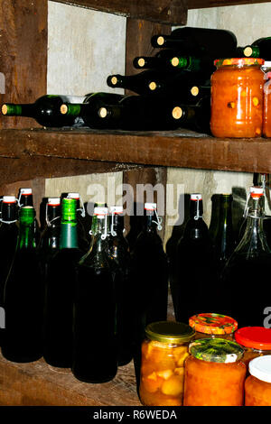 homemade wine in bottles in home basement, with jam, salad jars Stock Photo
