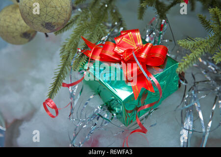 Green gift box with out of focus lights on a snow background . Christmas green boxes with snow , christmas images, in blurred background. With a red ribbon Stock Photo