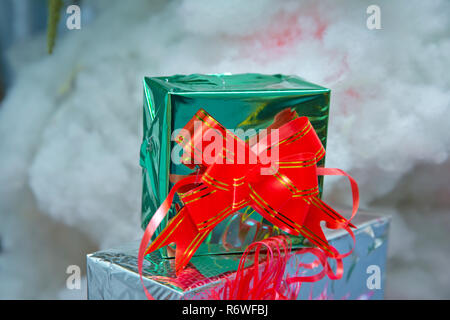 Green gift box with out of focus lights on a snow background . Christmas green boxes with snow , christmas images, in blurred background. With a red ribbon Stock Photo