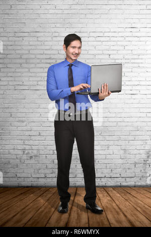 Young asian businessman standing while typing on laptop Stock Photo