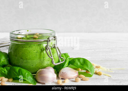 Pesto sauce in a jar with pine nuts, parmesan and garlic on white wooden table. close up Stock Photo