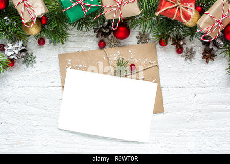 christmas blank greeting card with fir tree branches, decorations, red berries, gift boxes and cones over white wooden background. mock up. flat lay. Stock Photo