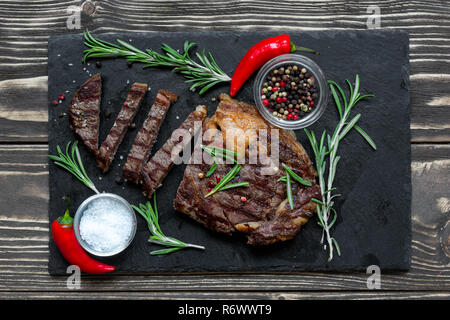 Beef steak with herbs and spices on black slate over wooden background. top view Stock Photo