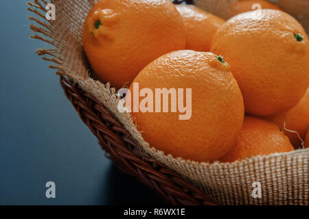 Bright orange tangerines (clementines) in wicker basket with burlap on a dark background Stock Photo
