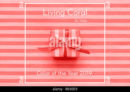 Living Coral color of the Year 2019 Gift box with bow on striped wrapping paper. Abstract geometric background. Stock Photo