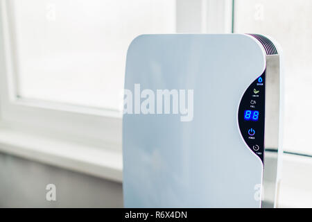 Dehumidifier with touch panel, humidity indicator, uv lamp, air ionizer, water container works by wet window in flat. Stock Photo