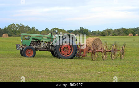 The old farm tractor sits idle in the field with hay rake attached.  The farmer has taken a brief break from baling hay on a hot summer day in Missour Stock Photo