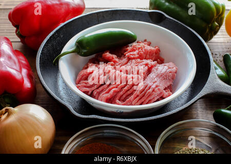 Raw ground beef inside skillet with peppers and other cooking ingredience around with wooden background side view Stock Photo