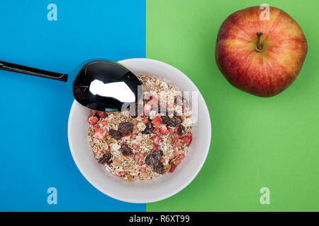 muesli in white bowl on blue and green ground with spoon and apple Stock Photo