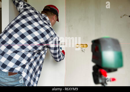 lueing wallpapers at home. Young man, worker is putting up wallpapers on the wall. Home renovation concept Stock Photo
