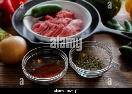 Raw ground beef inside skillet with peppers and other cooking ingredience around with wooden background side view Stock Photo