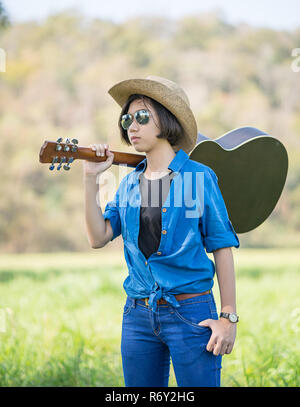 Woman wear hat and carry her guitar in grass field Stock Photo