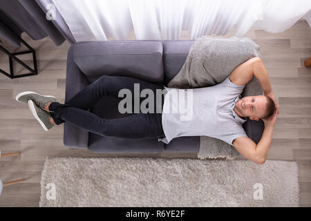 High Angle View Of A Smiling Young Man Resting On Sofa Stock Photo