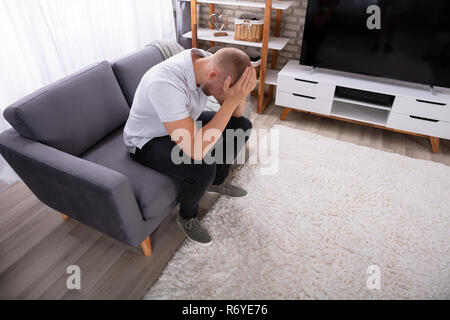 Side View Of A Upset Young Man Sitting On Sofa Stock Photo