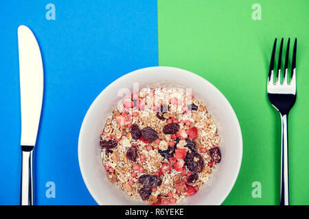 muesli in white bowl on blue and green ground with knife and  fork Stock Photo