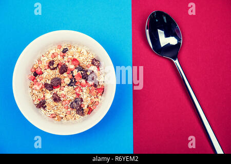 muesli in white bowl on blue and red ground with spoon Stock Photo