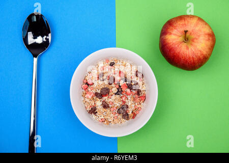 muesli in white bowl on blue and green ground with spoon and apple Stock Photo