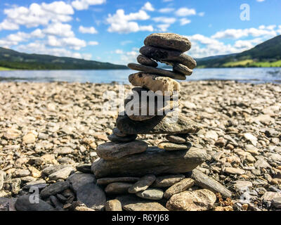Close-up of stone cairn on a pebble beach with mountains and lake in the background Stock Photo