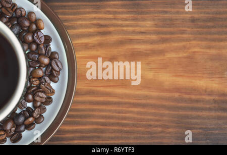 A cup of coffee on a saucer with fried coffee beans, placed on the left. Stock Photo