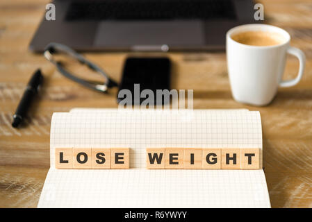 Closeup on notebook over wood table background, focus on wooden blocks with letters making LOSE WEIGHT words Stock Photo