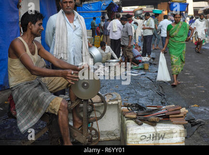 A knife sharpener at work using a whetstone or sharpening wheel propelled via pedals an a bicycle mechanism, at a fish market in Mumbai, India Stock Photo