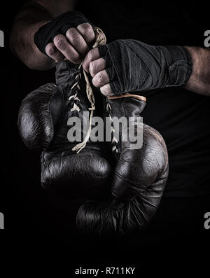 pair of very old boxing sports gloves in men's hands rewound with a black bandage Stock Photo