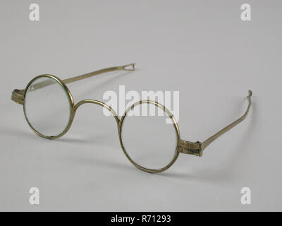 Glasses with round lenses on strength, frame of brass with wide bridge and hinged springs that end in loop shape, spectacle eye lens equipment glass copper base metal, glass, Glasses with round lenses on strength. The frame and the bridge is one piece and of brass The bridge is thin but wide. The flat narrow straight springs are fixed to the frame. The spring ends in small loop shape seeing eyesight-farsighted eye drift correction Stock Photo