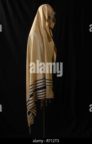 Jewish prayer scarf or tallit gadol of white silk with gold and silver embroidery, tallith liturgical clothing men's clothing apparel silk gold silver, textile appliqué White silk cloth with blue webs woven on one side and piece of silver brocade lace of about 35 cm long on the other side. Seven blue strips have been woven around and there are two rectangular pieces of fabric with gold embroidery. In these patches is hole for button cord to do. cardboard number is sewn on the strips. Along the short side are leftovers of frills made from the fraying of the fabric religion Judaism judaica praye Stock Photo