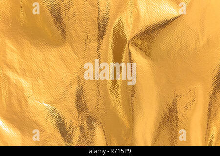 Highly detailed texture of a rusty golden yellow shimmering thermal blanket background. Stock Photo
