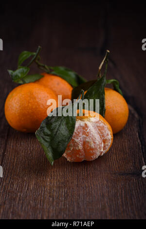 Three fresh tangerines with leaves and one half peeled on a wood Stock Photo