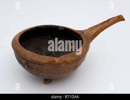 Pottery saucepan on three legs, with pouring lip and handle, inward curled upper edge, saucepan pan crockery holder kitchenware earth discovery ceramics earthenware glaze lead glaze, hand-turned molded glazed baked Pottery saucepan with semi-circular body on three legs Slanted upwards scalloped handle Curled top edge with pouring lip. Red shard entirely glazed. Rotations on the shoulder. Burnt food remains on the inside archeology indigenous pottery cooking kitchen food preparation Stock Photo