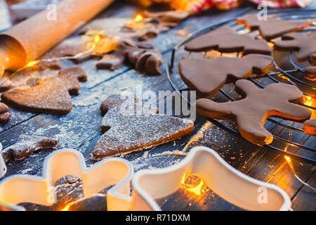 Gingerbread Christmas cookies in shape of trees, sprinkled with powdered sugar on a wooden table with warm orange glow from Christmas lights Stock Photo